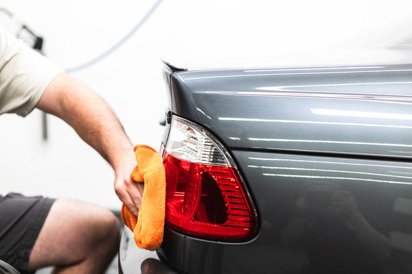 Armour Detail Ceramic being wiped on grey car tail lights with orange FTW towel.
