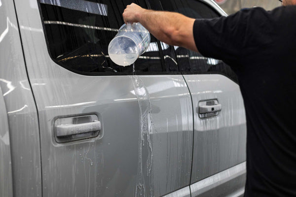 A person pouring water on to a grey truck.