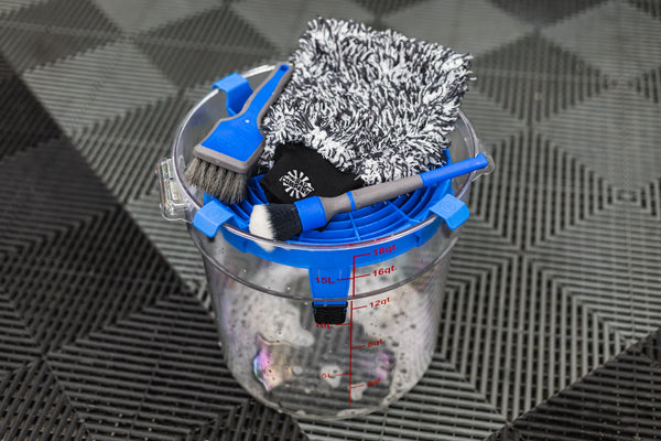 Detail Factory Clean Screen Avalanche placed on top of a clear wash bucket, holding detailing brushes and a microfiber wash mitt.