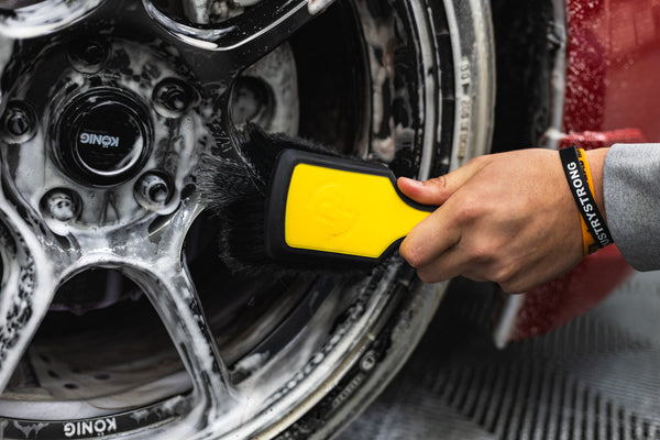 A person using a Detail Factory Wheel Face Brush Livewire to clean a red vehicle's tire.