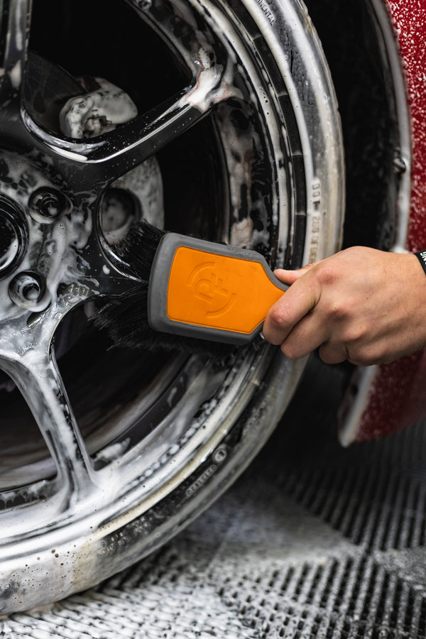 A person using a Detail Factory Wheel Face Brush Solar Flare to clean a red vehicle's tire.