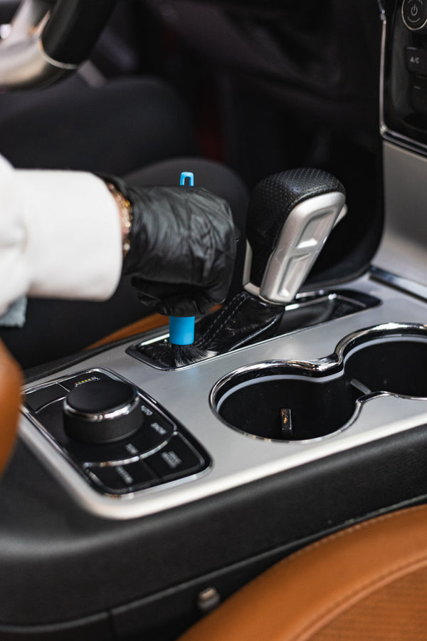A person cleaning the shifter of a vehicle with a riptide crevice brush.