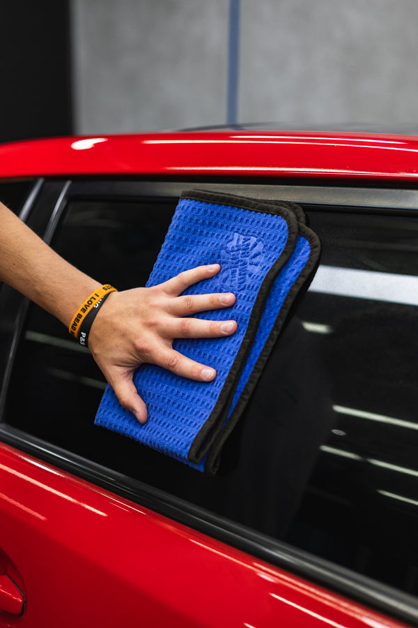 Person cleaning a car window with a navy blue 16x24 dry me a river microfiber towel.