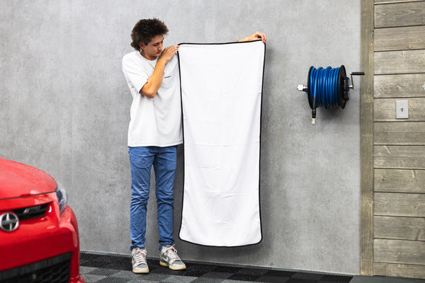 Person holding a white 26x59 dry me a river microfiber towel next to a red car.