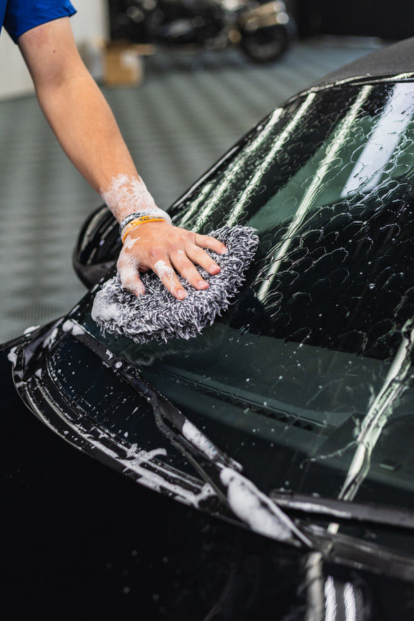 Person washing a black car with a soapy sponge with KochChemie NanoMagic Shampoo on it.