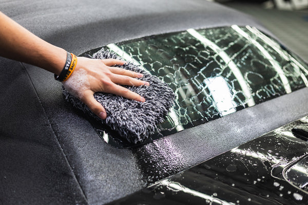 Person cleaning a car window with a microfiber pad