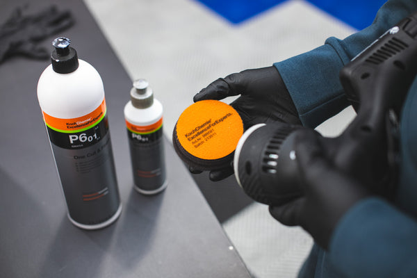 A person attaching a KochChemie One Cut and Finish Pad to a Rupes Polisher with two bottles in the background.