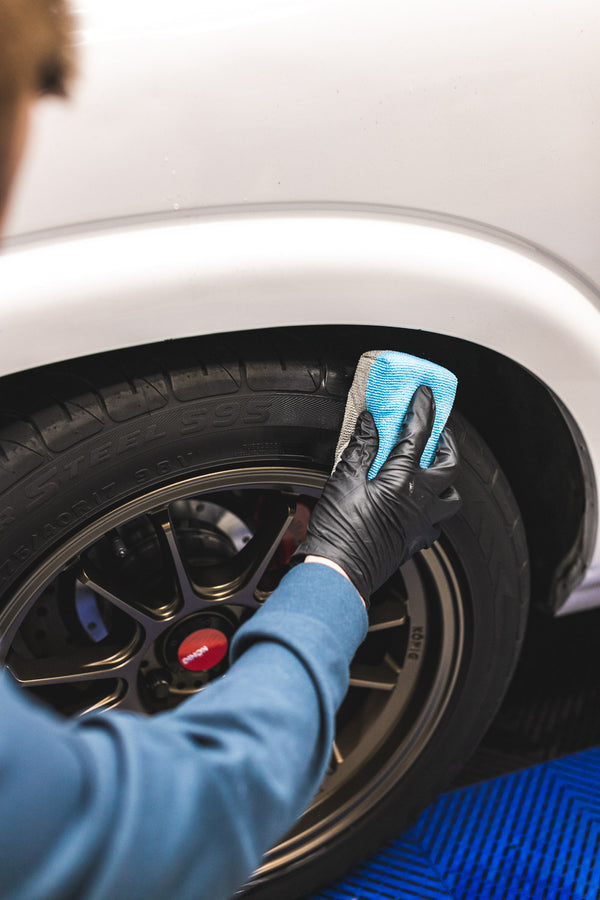 Person cleaning a car tire with a blue sponge and black gloves.