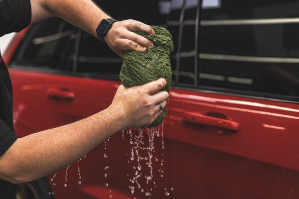 Person holding a green m22 with water dripping from it in front of a red car.