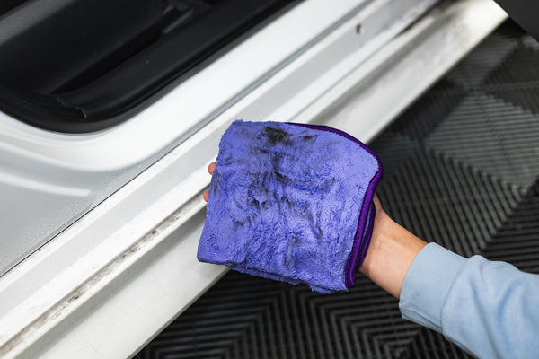 Person cleaning a car with a purple minx royale microfiber towel