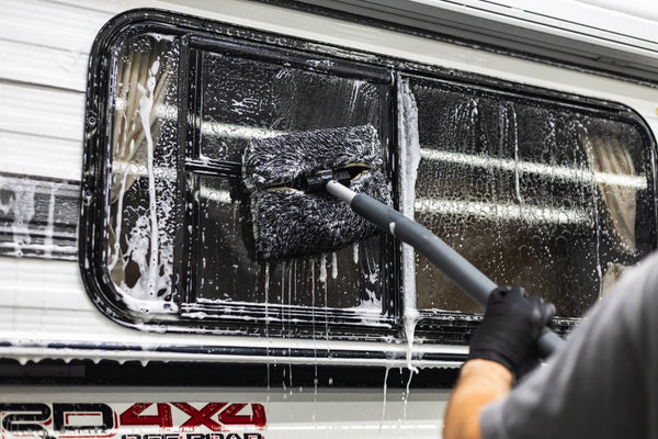 A person cleaning the window of a camper with a mitt on a stick