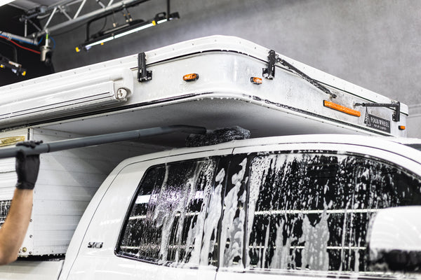 A person cleaning the roof of a truck with a mitt on a stick.