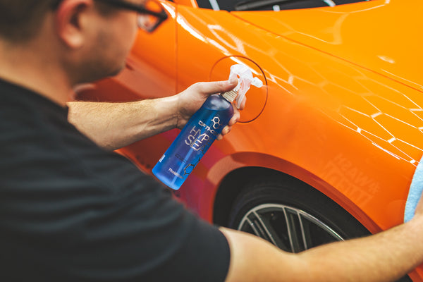 Person cleaning an orange car with a bottle of Opti-Coat Hyper Seal.