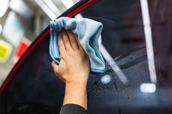 Person cleaning a car window with a blue FTW microfiber.