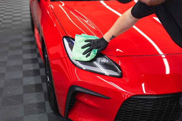 Person cleaning a car front headlight with a green FTW microfiber.