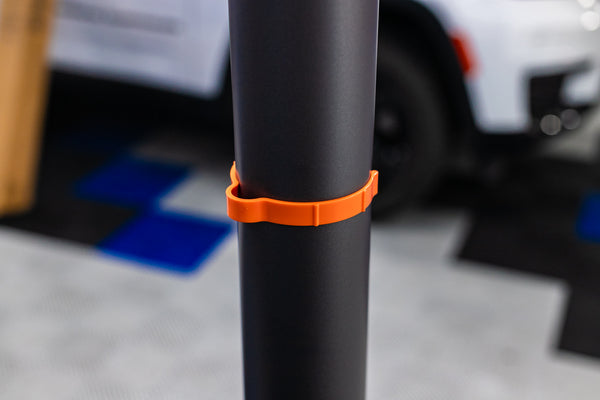 A orange Yellotool Speedclip on a black pole with a car in the background.