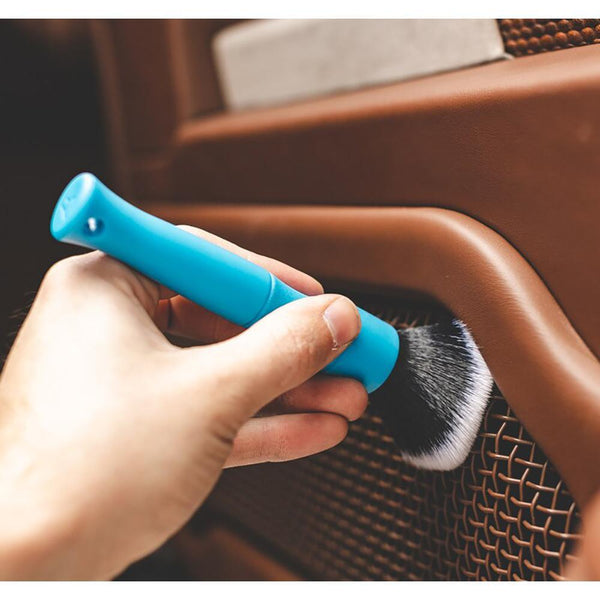 A close up of a person cleaning the interior of a car door with a blue Synthetic Detailing Brush.