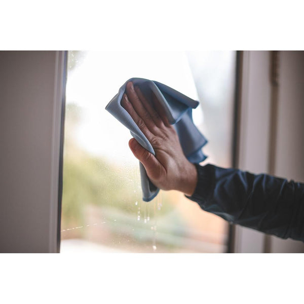 A closeup of a person wiping a glass back door with a window towel.