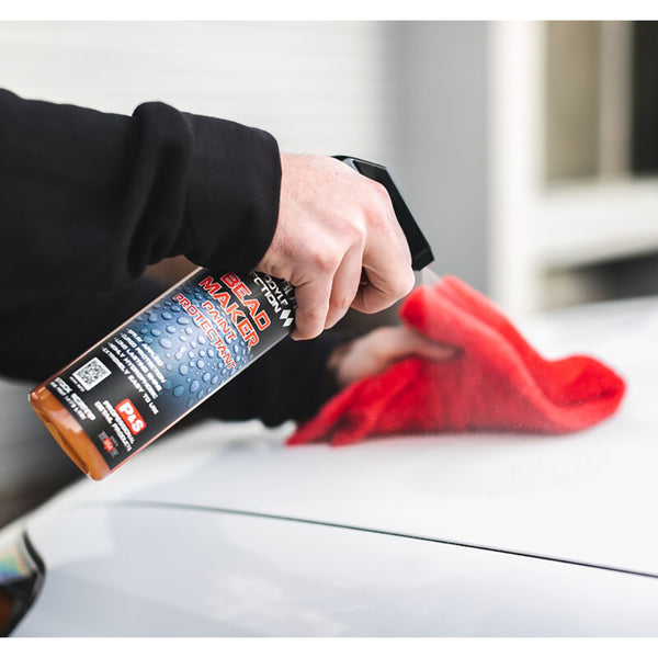 A closeup of a person spraying P&S Bead Maker onto a white car hood and wiping it with a red towel.