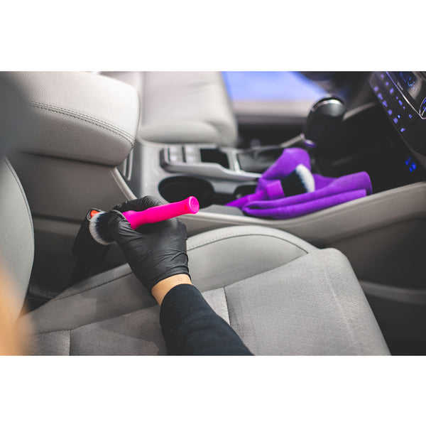 A closeup of a person detailing a seatbelt with a purple synthetic detailing brush.