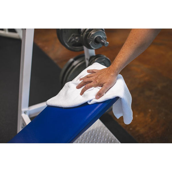A closeup of person wiping a weight bench with a white Spa and Workout towel.