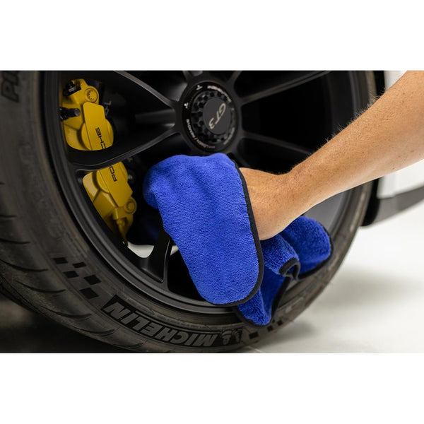 A person scrubbing a car tire rim with a blue microfiber Spectrum towel.