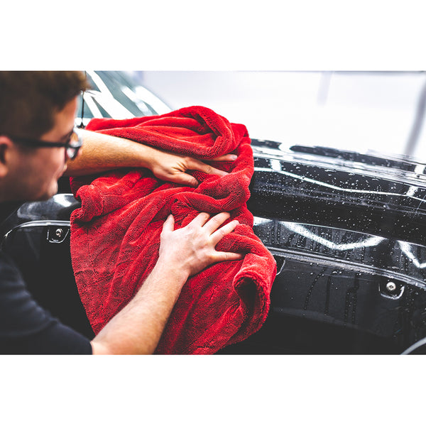 A person cleaning the front of a black car with a red 1500 towel.