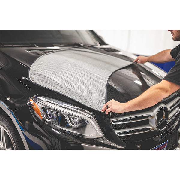 A closeup of someone spreading a grey big one towel across the hood of a car.