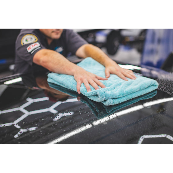 A closeup of a person wiping the roof of a black car with a folded liquid8r towel.