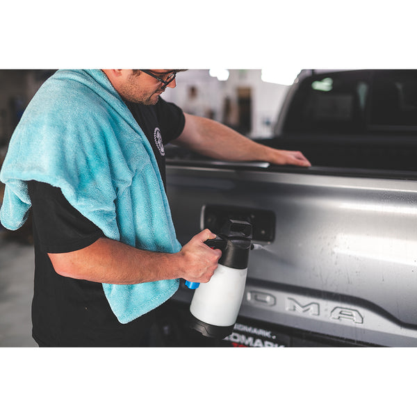 A person spraying the back of a truck with an IK sprayer with a liquid8r towel thrown over their shoulder.