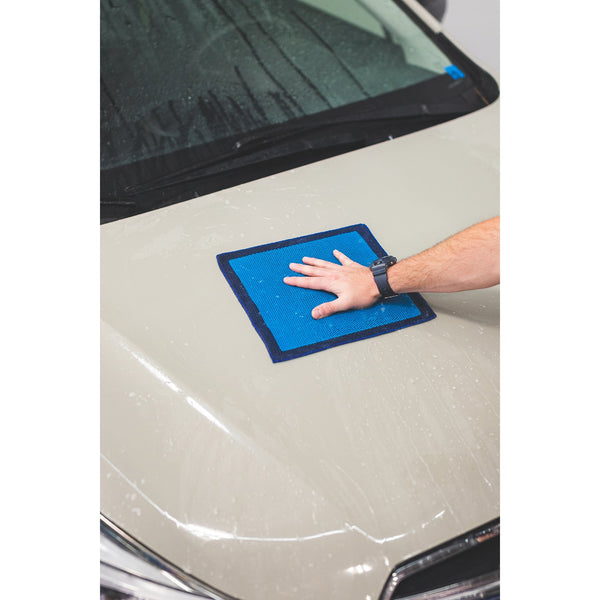 A closeup of a person cleaning the hood of a beige hood with an Ultra Clay towel.