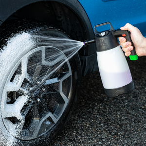 A person spraying foam onto the tire of a blue car with the IK Foam Pro 2.