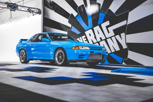 A blue car in an autobody shop with a The Rag Company logo on the wall behind the car.