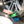 A hand holding a short green Wheel and Body brush cleaning a foamy car tire rim.