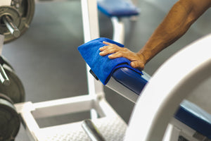 A person cleaning gym equipment with a royal blue all purpose towel.