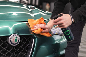 A person spraying Armour Detail Supply Amplify onto a car while holding an orange microfiber.