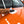 A closeup of a person cleaning the hood of an orange car with a while paper towel.