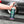 A person holding a spray bottle of Armour Tire Cleaner in front of a grey car.