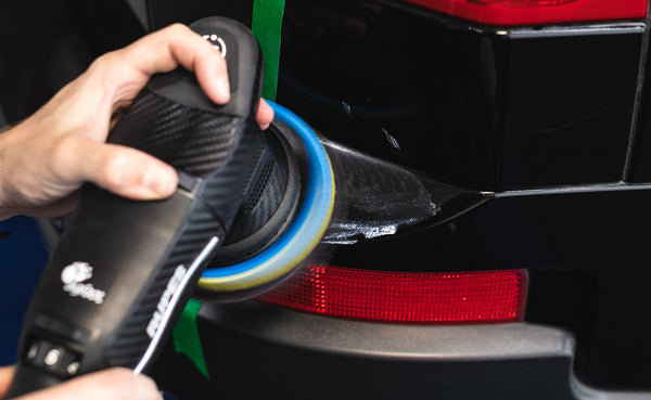 A person using a Rupes Polisher on the back of a black vehicle.