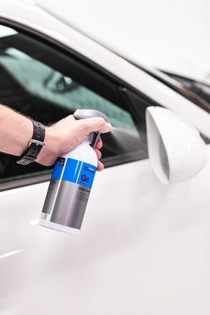 Koch-Chemie Glass Cleaner sprayed onto side glass mirror of a white car. 