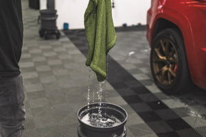 Green m22 towel dripping into a grey bucket on a checkered floor with a red car in the background.