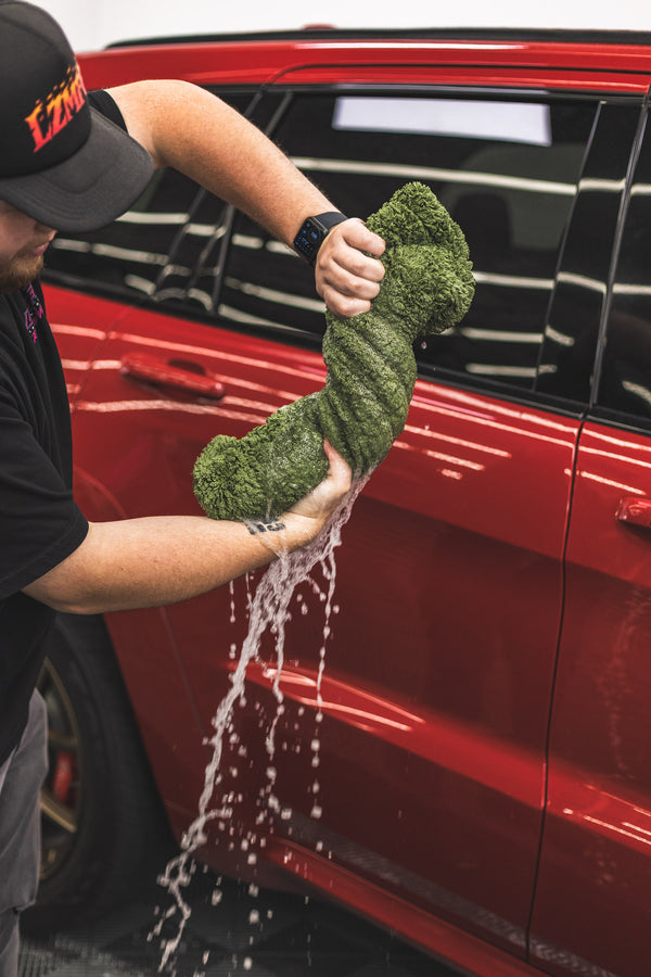 Person holding a green m22 with water dripping from it in front of a red car.