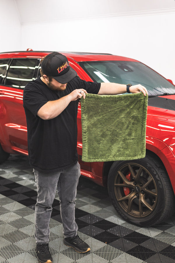 Person holding a green m22 towel in front of a red car on a checkered floor.