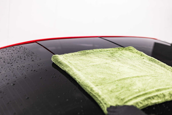 Green microfiber towel on a car's black surface with water droplets.