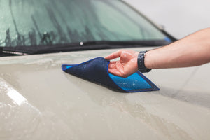 A wet hand flipping over a blue Ultra clay towel on the hood of a car.