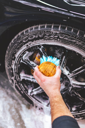 A person using a TRC Ultra Utility Brush to clean a tire covered in foam.