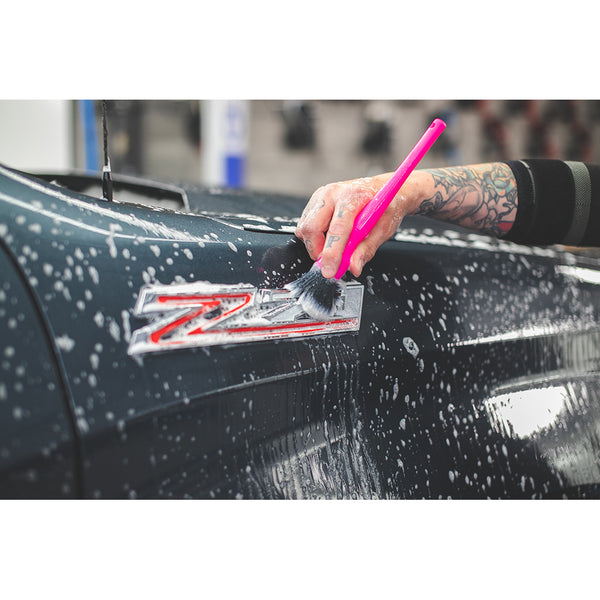 A closeup of a person cleaning the emblem on the side of their truck with a pink synthetic detailing brush.