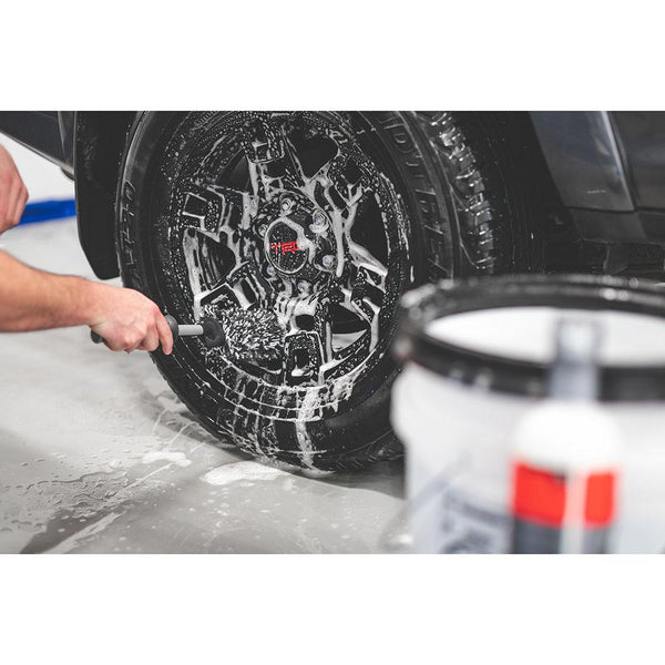 A closeup of a person scrubbing a foam covered tire with a wheel brush.