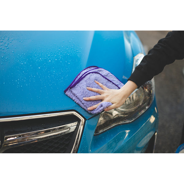 A closeup of a person wiping a blue car with a Minx Royal towel.