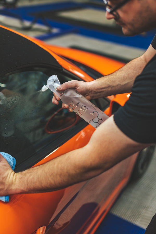 A person spraying the window of an orange porsche with Opti-Coat Glass Cleaner. 